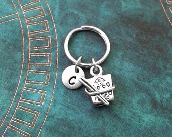 May include: Silver keychain with a charm of a takeout container with chopsticks and the word "FOOD" on it. The keychain also has a silver charm with the letter "C" on it.