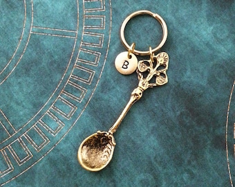 May include: Gold-toned spoon keychain with a decorative floral design and a round charm with the letter "B" on a teal background.
