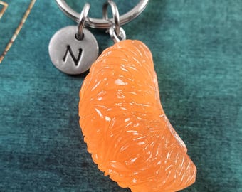 May include: A silver keychain with a round charm that says "N" and a 3D orange slice charm. The orange slice charm is a realistic depiction of a mandarin orange segment.