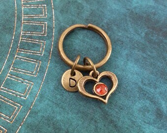 May include: A bronze key chain with a heart charm featuring a red rhinestone. The charm also has a letter 'D' on a round disc.