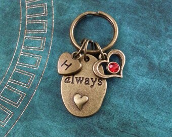 May include: A bronze key chain with a heart charm, a charm with the letter H, and a charm with the word "always" engraved on it. The heart charm has a red rhinestone in the center.