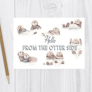 May include: A white card with a watercolor illustration of otters in various poses. The text "Hello from the otter side" is written in black lettering.