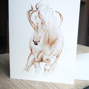 May include: A watercolor painting of a horse in shades of brown and white. The horse is depicted in a dynamic pose, with its head lowered and mane flowing. The artwork is on a white card.
