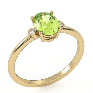 Può includere: Un anello d'oro con una grande pietra preziosa ovale di peridoto verde e due diamanti rotondi più piccoli sui lati.