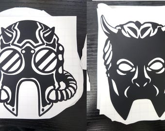 Pode incluir: Dois adesivos de vinil preto e branco, um de uma máscara de gás com chifres e o outro de uma máscara do diabo.