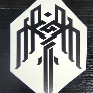 May include: A white sticker with a black geometric design. The design features a central shape that resembles a sword with wings.