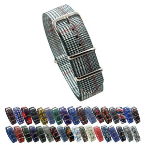 Peut inclure: Un bracelet de montre à motif gris et blanc avec des accents rouges et une boucle argentée. Le bracelet est en tissu tissé et a un look classique. Le bracelet est présenté avec une variété d'autres bracelets de montre à motifs en arrière-plan.