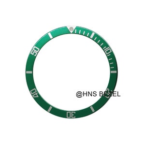 May include: A green watch bezel with white markings and numerals. The bezel has a circular design with numbers indicating time increments. The text "@HNS BEZEL" is visible on the lower right.