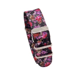 Pode incluir: Uma pulseira de relógio preta com estampa floral em tons de rosa, roxo e verde. A pulseira tem uma fivela prateada com o texto "HNS" gravado nela.