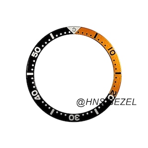 Op de afbeelding: Een zwarte en gouden horzel met witte cijfers en markeringen. De horzel is verdeeld in twee secties: zwart met witte cijfers en goud met witte markeringen. De tekst "@HNS BEZEL" is zichtbaar.
