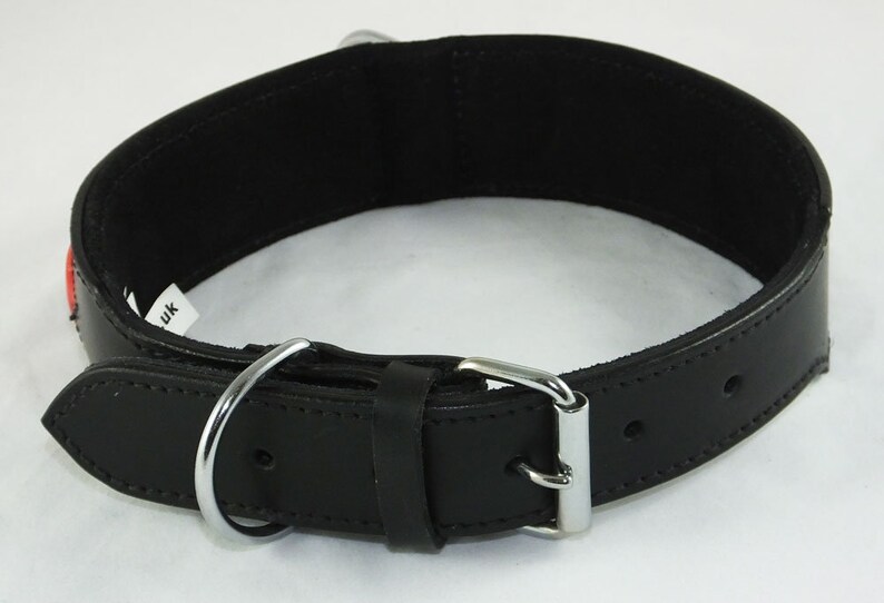 May include: Black leather dog collar with a silver buckle and a silver D-ring. The collar has two rows of stitching and a small red label that says "UK".