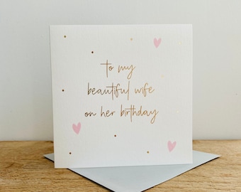 May include: A white card with gold lettering that says "To my beautiful wife on her birthday". The card has pink hearts and gold dots scattered across the front.