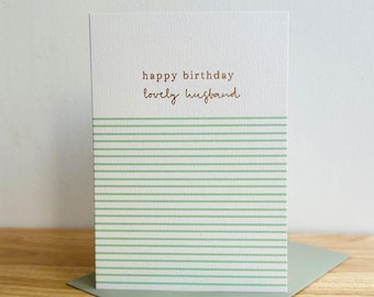 Puede incluir: Una tarjeta de felicitación blanca con una superficie texturizada que presenta el texto "happy birthday" en una fuente sencilla y "lovely husband" en letra cursiva. La parte inferior de la tarjeta está decorada con numerosas líneas horizontales finas de color verde claro.