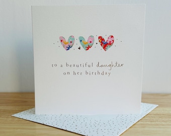 Puede incluir: Una tarjeta blanca con tres corazones coloridos y el texto "a una hermosa hija en su cumpleaños".