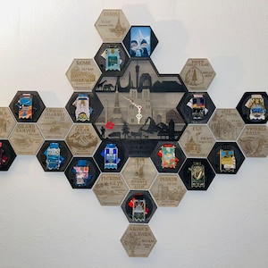 May include: A wooden wall art piece with a clock and hexagonal frames. Each frame displays a travel destination, pins, and distance. The central frame features a silhouette of a city skyline. The clock has a silver-colored pendulum.