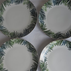 May include: Set of four white ceramic dinner plates with a green and blue tropical leaf design.
