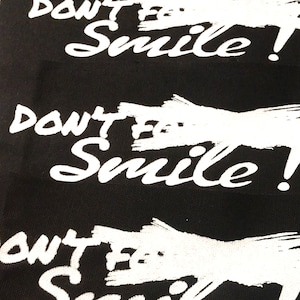 May include: Black fabric patches with the text "DON'T F* Smile!" in white. A small pink card with a skull illustration is on top. A business card with the text "BRUJAS Y VAMPIROS" is at the bottom.