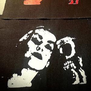 Può includere: Tre toppe di tessuto nero con immagini serigrafate in bianco e rosso di un teschio e ossa incrociate. La toppa superiore ha un teschio e ossa incrociate bianche, la toppa centrale ha un teschio e ossa incrociate rosse, e la toppa inferiore ha un teschio e ossa incrociate bianche.