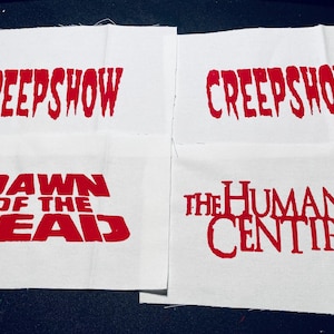 Puede incluir: Cuatro cuadrados de tela blanca con texto rojo. El texto dice "Creepshow", "Dawn of the Dead", "Creepshow" y "The Human Centipede".