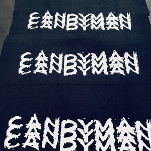 Op de afbeelding: Vier zwarte stoffen patches met het woord "CANBYMAN" in wit gedrukt, in een gestileerde lettertype met een gekartelde, handgetekende look.