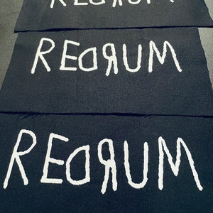 Op de afbeelding: Drie zwarte stoffen patches met het woord "REORUM" in wit op elke patch.