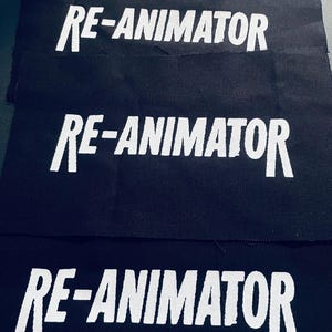 May include: Four black fabric patches with the white text "RE-ANIMATOR" in a stylized font.