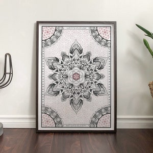 Op de afbeelding: Een zwart-wit mandala-print met een roze centrum, ingelijst in een donkerhouten lijst. De print is op een witte achtergrond en heeft een geometrisch ontwerp.