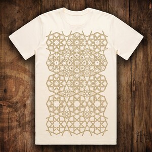 May include: A white t-shirt with a geometric pattern in gold on the front. The pattern is made up of repeating shapes that resemble stars and flowers.