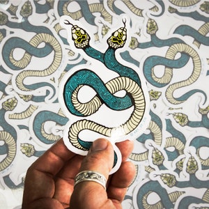 May include: A sticker featuring a two-headed snake with a teal and cream patterned design. The snake is curled into a figure eight shape. The sticker is on a white background.