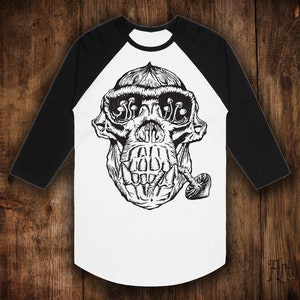 Op de afbeelding: Een wit en zwart baseballshirt met een zwart-witte illustratie van een apenkop met paddenstoelen in zijn ogen en een pijp in zijn mond.
