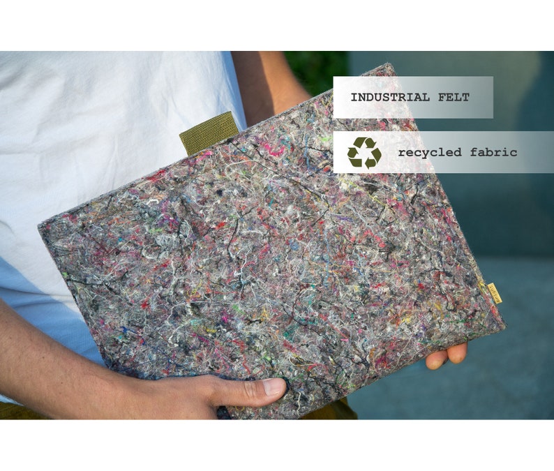 May include: A rectangular laptop sleeve made of industrial felt and recycled fabric. The sleeve is gray with colorful flecks of red, pink, blue, and green. A green fabric tab is attached to the top edge. The text "INDUSTRIAL FELT" and "recycled fabric" are visible.