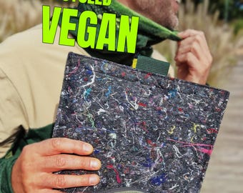 Könnte beinhalten: Eine dunkelgraue, rechteckige, recycelte vegane Laptoptasche mit bunten Flecken. Die Tasche wird vor einem grünen Rucksack gehalten. Die Worte "RECYCLED VEGAN" stehen in leuchtend grüner Schrift.