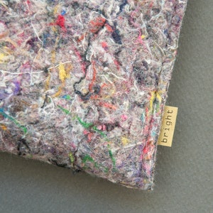 May include: Close-up of a gray, textured fabric with colorful threads of red, yellow, green, and purple. A small, rectangular tag with the word "bright" is attached to the fabric.