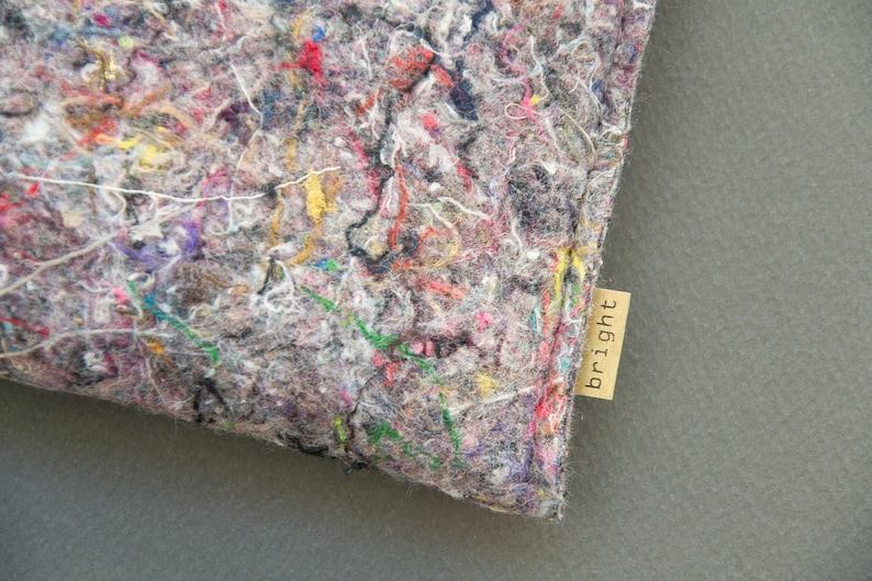 May include: Close-up of a gray, textured fabric with colorful threads of red, yellow, green, and purple. A small, rectangular tag with the word "bright" is attached to the fabric.