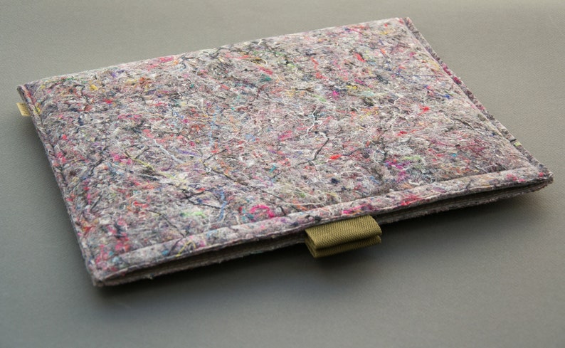 May include: Rectangular laptop sleeve with a speckled, multi-colored design. The sleeve is primarily gray with flecks of pink, blue, and yellow. It has a stitched border and a green fabric loop on the bottom right corner.