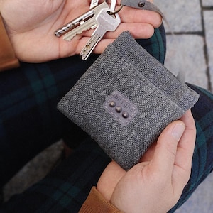 May include: A grey fabric key holder with a leather patch bearing the word "bright" and three small rivets. A person holds the key holder and a set of keys.