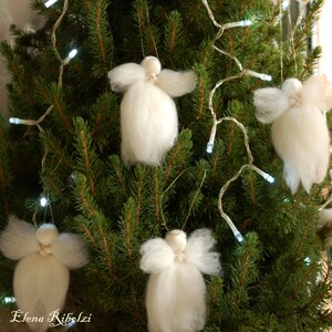 Op de afbeelding: Een kerstboom versierd met witte engelenornamenten en lichtslingers. De handgemaakte engelen zijn gemaakt van witte wol en hebben een eenvoudig ontwerp. De boom is van nature groen en de lampjes zijn klein en wit.