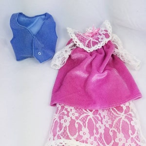 May include: A pink and white doll's dress with a blue waistcoat. The dress has a lace overlay and a pink velvet bodice. The waistcoat is a solid blue colour.