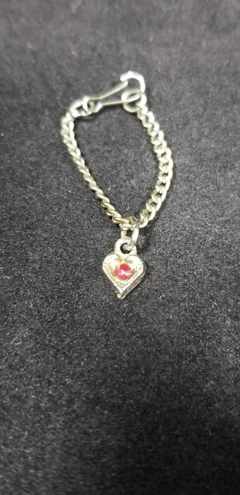 May include: A silver chain necklace with a heart-shaped pendant. The pendant has a red gemstone in the center.