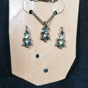 May include: A silver necklace and earrings set with a small, clear stone in the center of each piece. The jewelry is displayed on a tan card.