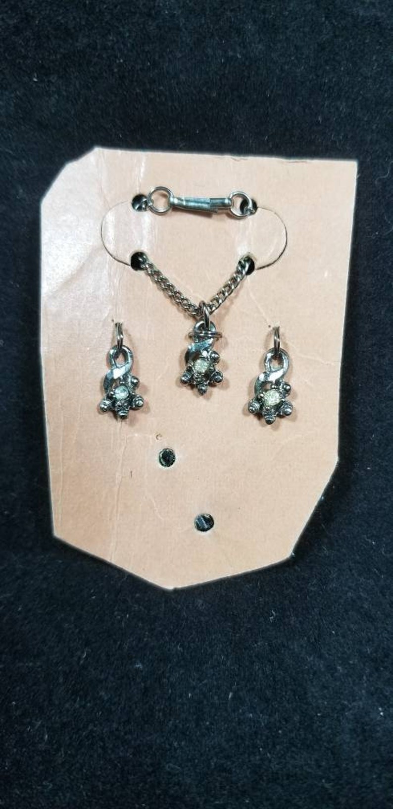 May include: A silver necklace and earrings set with a small, clear stone in the center of each piece. The jewelry is displayed on a tan card.