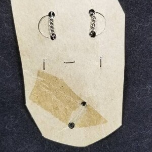 May include: A pair of silver earrings with a chain link design on a white card with a brown paper backing.