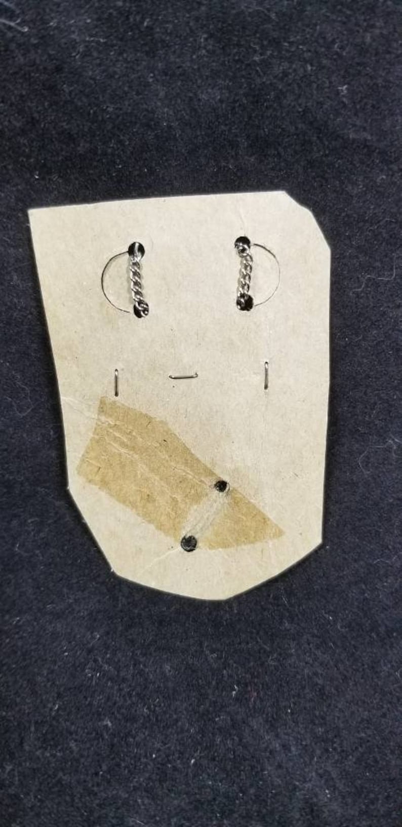 May include: A pair of silver earrings with a chain link design on a white card with a brown paper backing.