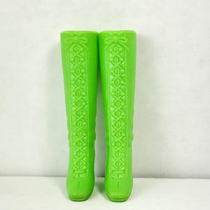 Puede incluir: Un par de botas altas de color verde lima con un diseño de encaje y un detalle de lazo en la parte superior.