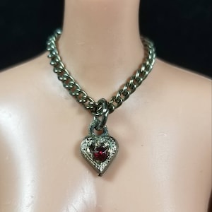 May include: A silver chain necklace with a heart-shaped pendant featuring a red gemstone.