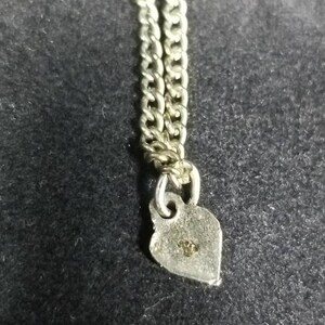 May include: A silver chain with a heart-shaped charm. The charm has a small inscription on the back.
