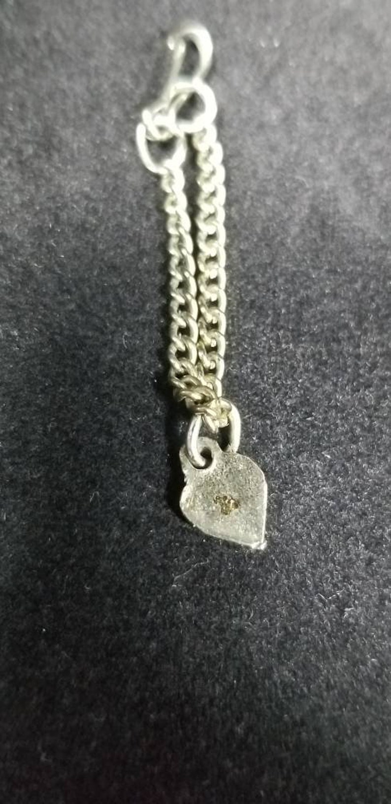 May include: A silver chain with a heart-shaped charm. The charm has a small inscription on the back.