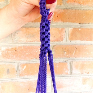 Puede incluir: Colgador de plantas de macramé morado con múltiples hebras y una parte superior anudada.