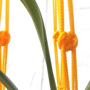 May include: Two yellow macrame plant hangers with knots at the top. The hangers are made of thick, braided rope.