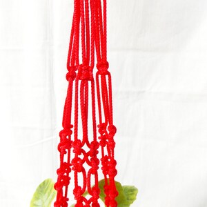 K&ouml;nnte beinhalten: Ein roter Makramee-Pflanzenh&auml;nger mit einem geknoteten Design. Der H&auml;nger besteht aus dickem, rotem Seil und ist perfekt zum Aufh&auml;ngen einer kleinen Pflanze.